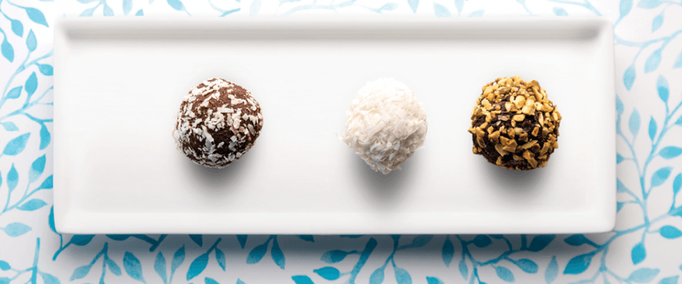 Three types of chocolate-covered nuts are arranged on a white plate, highlighting their diverse shapes and coatings.