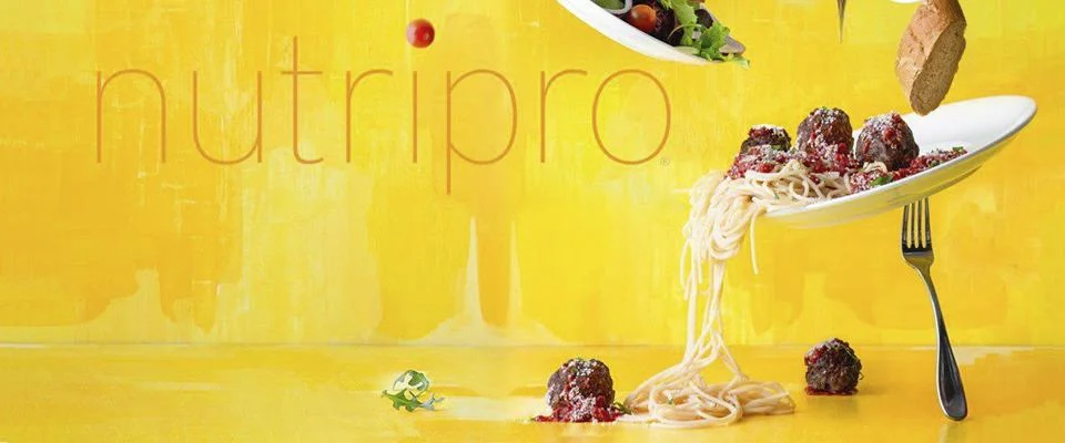 Spaghetti and meatballs falling off a plate with salad and bread on a yellow background.