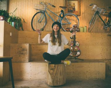 A woman on a stool poses in front of a bike, creating a relaxed and casual atmosphere.