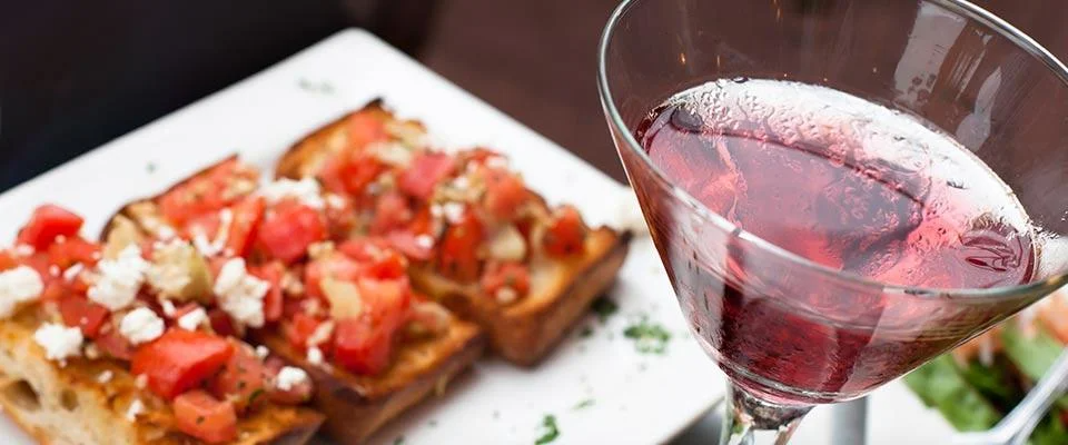 A glass of red wine beside a plate of gourmet food on a wooden table.