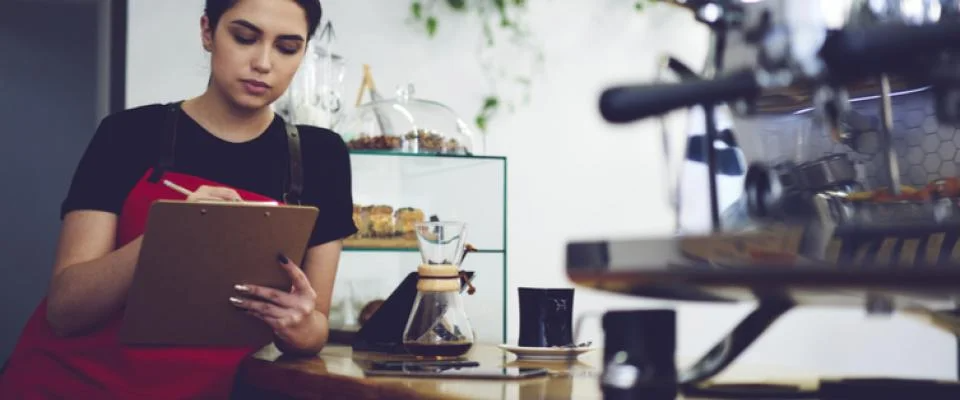 A woman in a café takes notes, following a 9-step checklist that showcases the planning process for opening a restaurant.