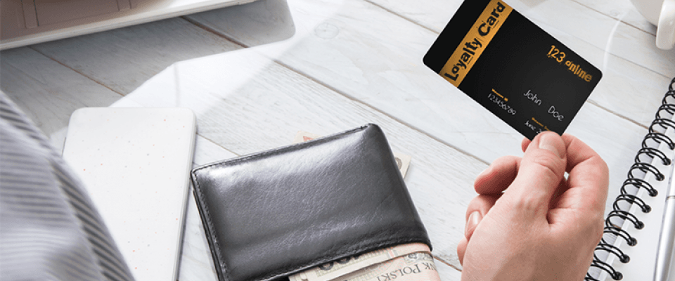 A hand holding a restaurant loyalty card next to a wallet with cash and a laptop.