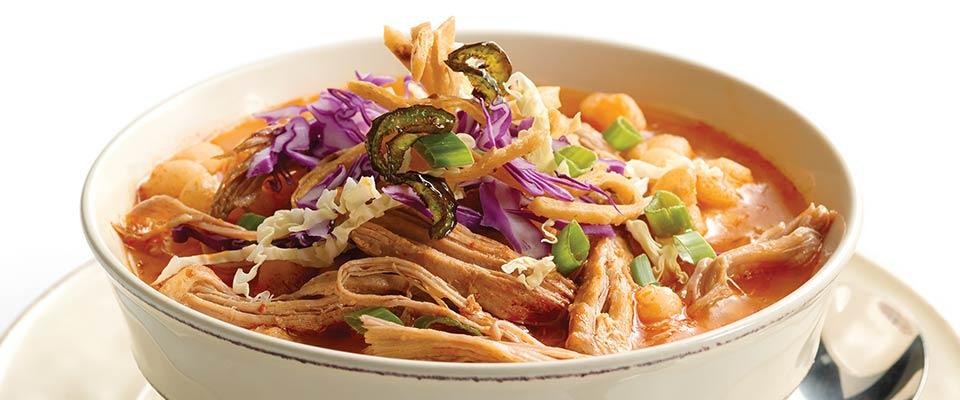A bowl of chili featuring shredded pork and a variety of colorful vegetables, garnished for a hearty meal.