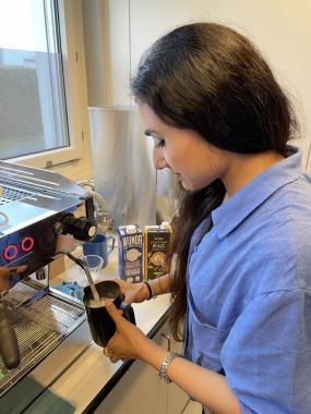 A woman in a blue shirt pours coffee into a coffee machine, preparing a fresh brew in her kitchen.