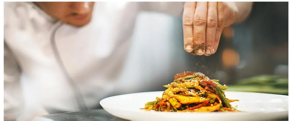A chef delicately sprinkles spices over a beautifully arranged plate of food, enhancing its flavor and presentation.