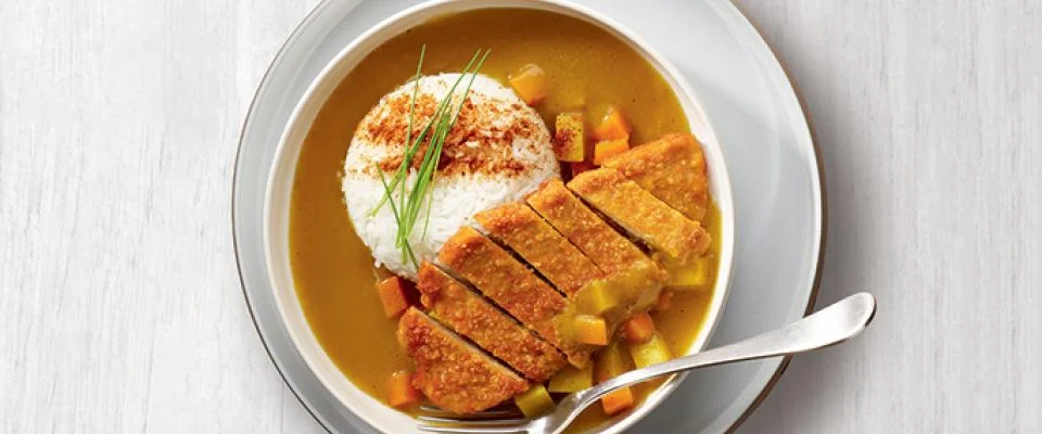 A bowl of curry served with rice and colorful vegetables, showcasing a vibrant and appetizing meal.