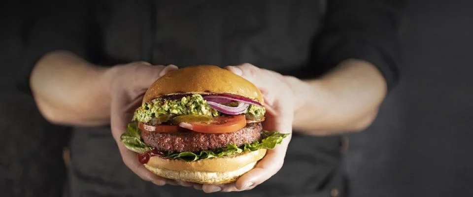 A person smiling while holding a delicious hamburger in both hands, ready to take a big bite.