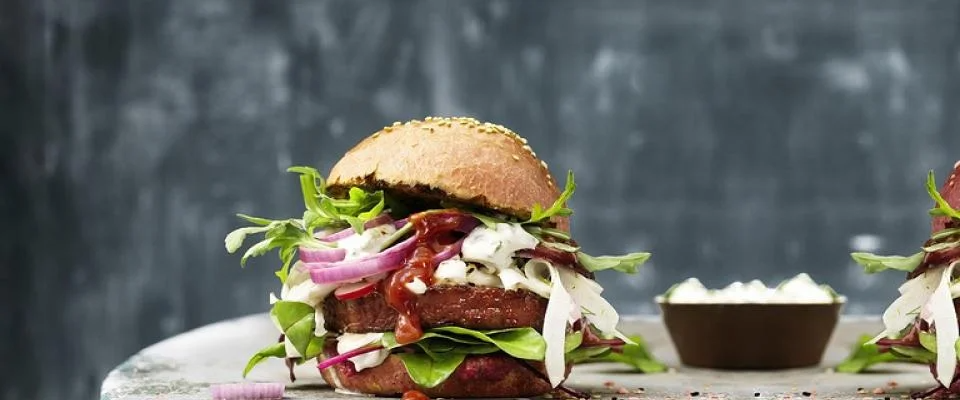 Two burgers on a table next to a bowl of sauce, ready to be enjoyed.