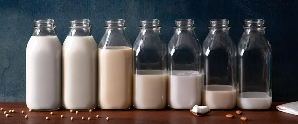 Variety of plant-based milks in glass bottles on a wooden table.
