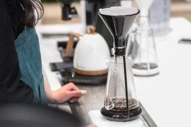 A person pours coffee grounds into a coffee maker, preparing to brew a pot of coffee.