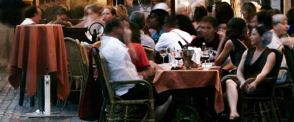 People enjoy meals at tables in a lively outdoor restaurant setting under clear skies.