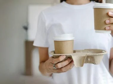 A woman is depicted holding two paper coffee cups, symbolizing a shared moment or a personal treat.