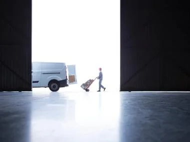 A man walks through an open door, approaching a parked van in a bright outdoor setting.