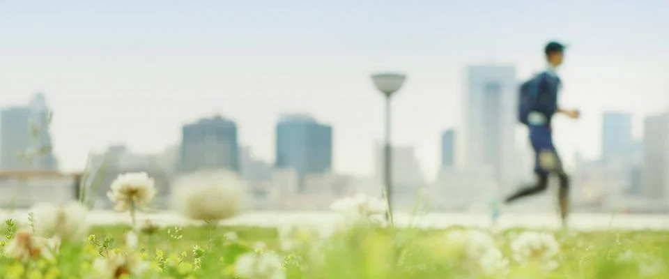 A man runs energetically in a green field, with a bustling cityscape rising in the background.