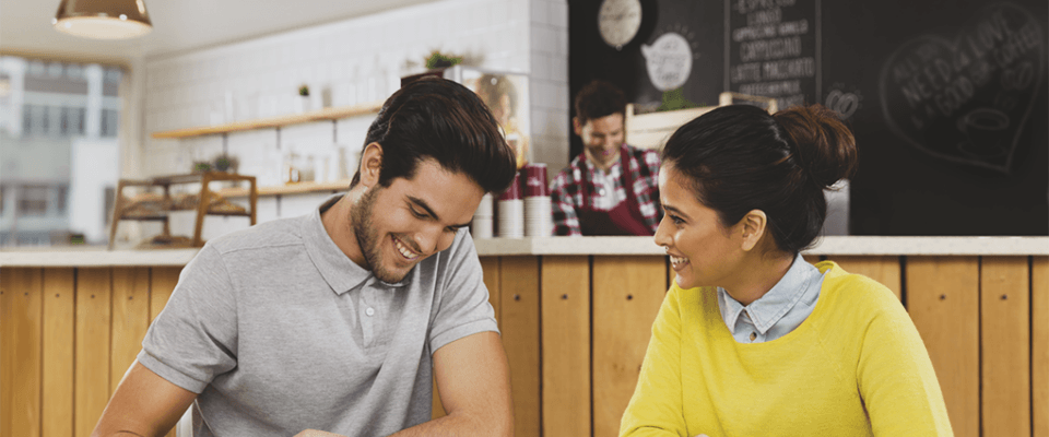 A man and woman are seated at a table, focused on a laptop in front of them.
