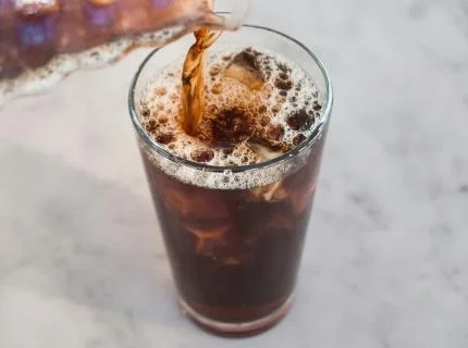 A glass of cola is being poured into a clear glass, creating bubbles and a refreshing look.