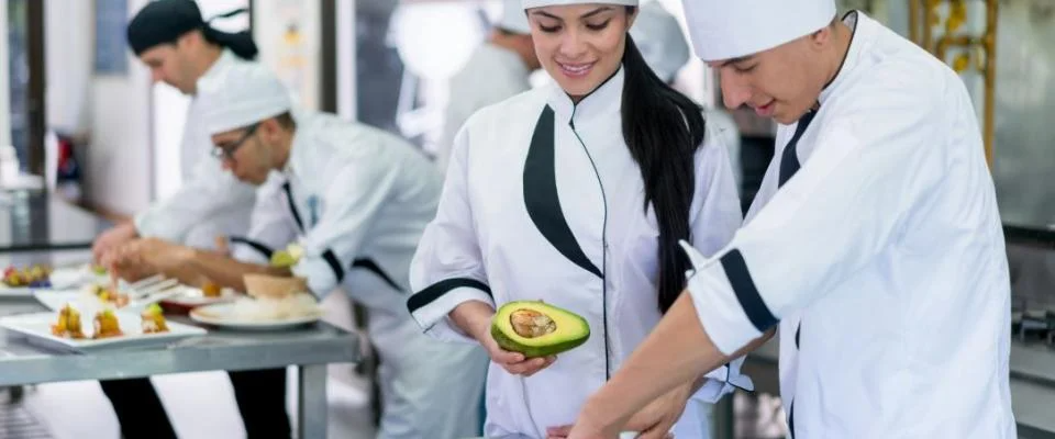 Chefs preparing dishes in a commercial kitchen filled with equipment and fresh ingredients.