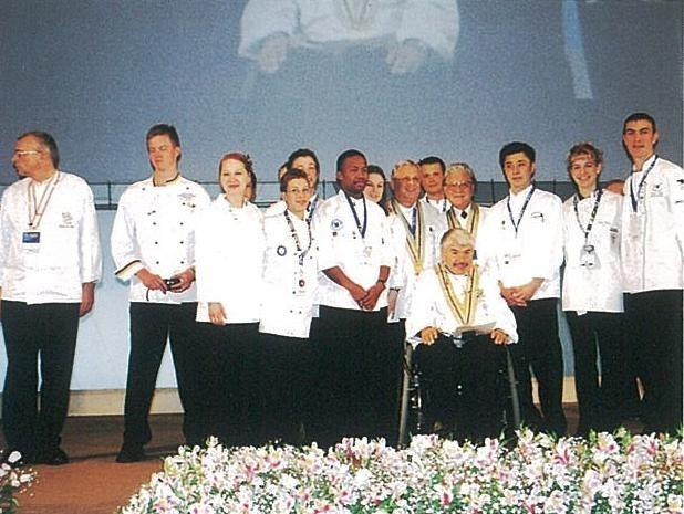 A group of people in white coats standing closely together, smiling and engaged in conversation.