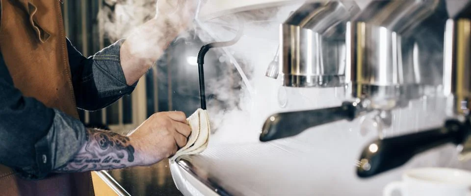 A barista cleans a steam wand, showcasing an essential feature for the best coffee machines.