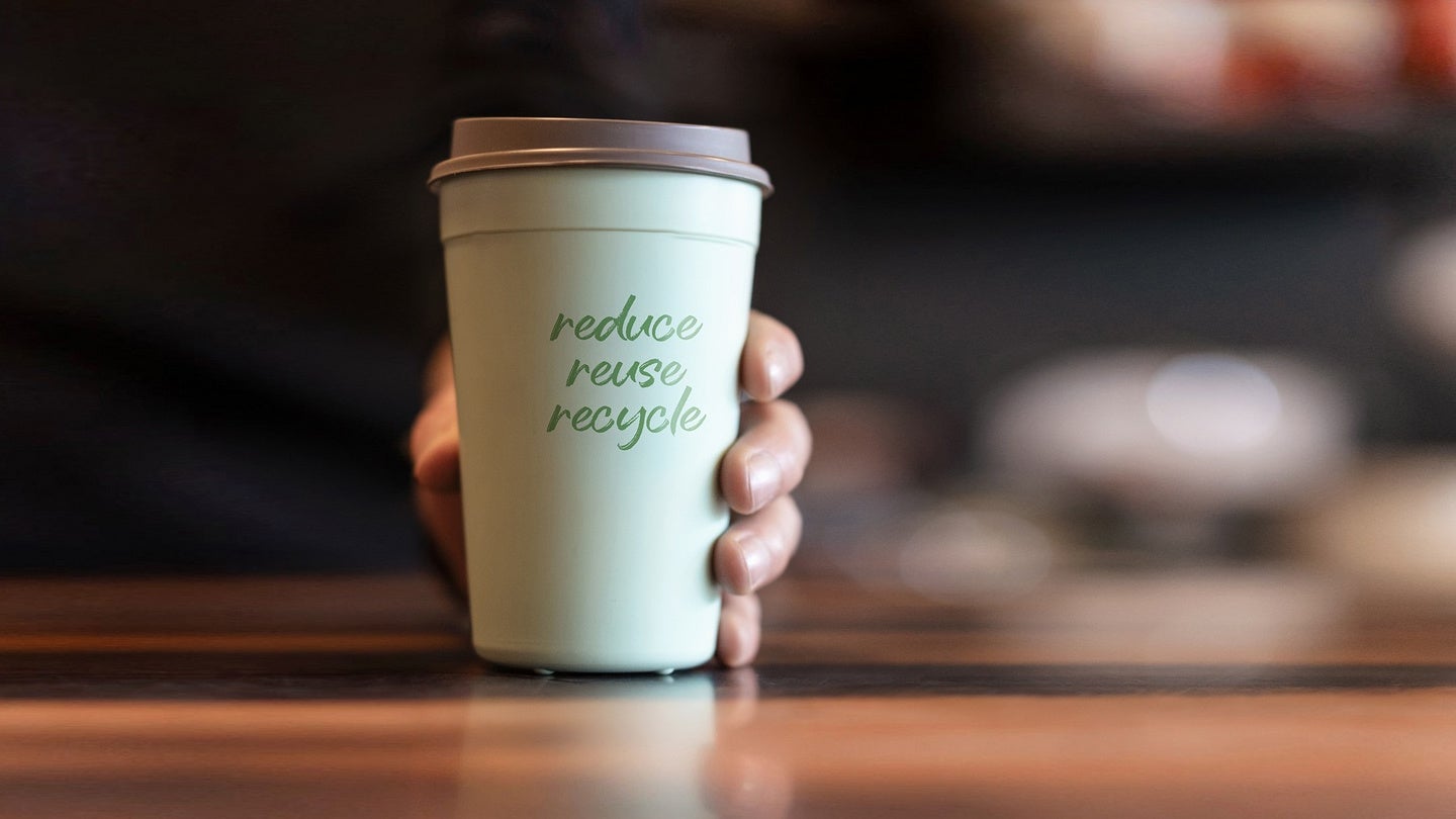 A person holds a green travel mug that says "make new friends" smiling.