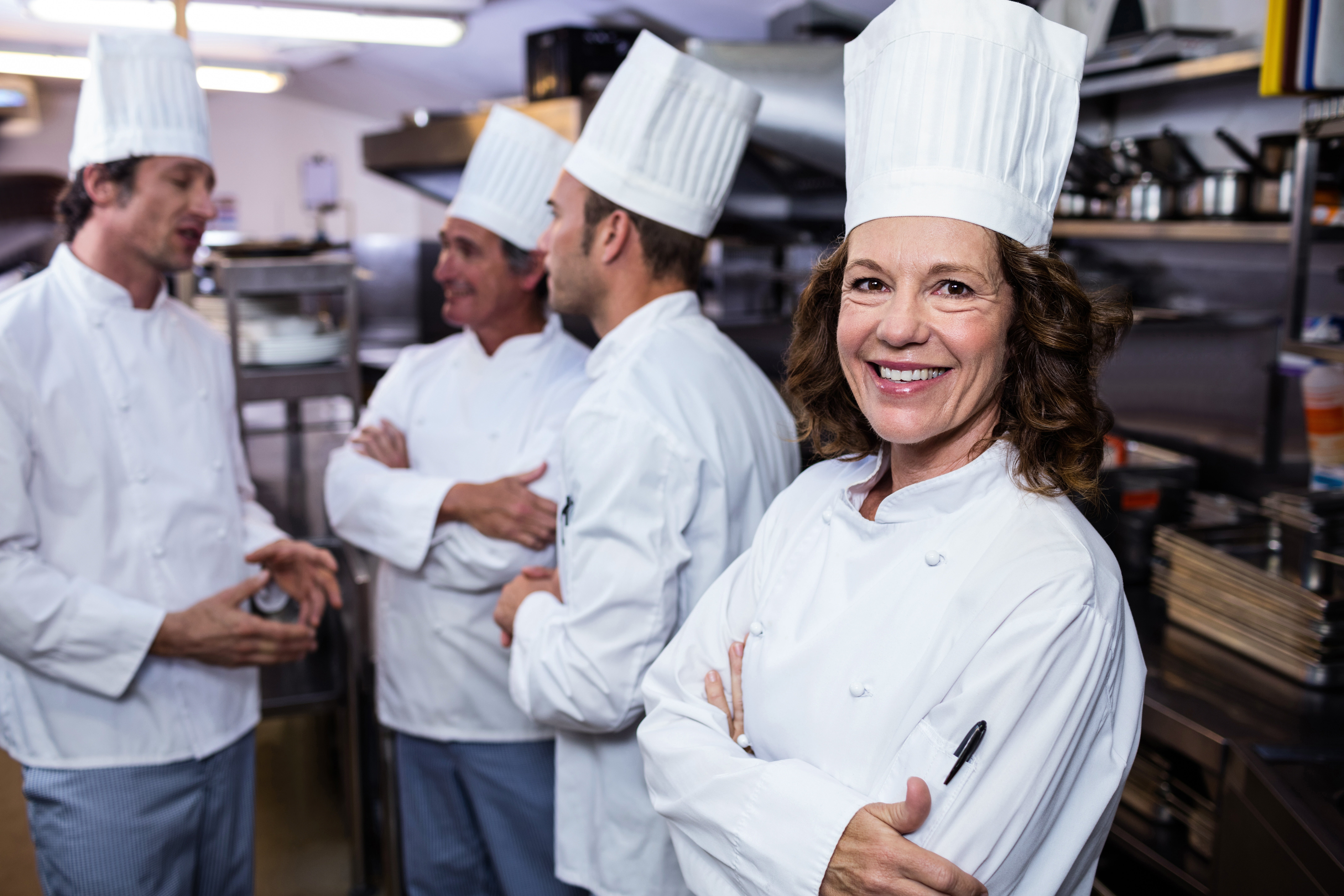 A group of chefs in white uniforms standing together in a busy kitchen, smiling and ready to cook.
