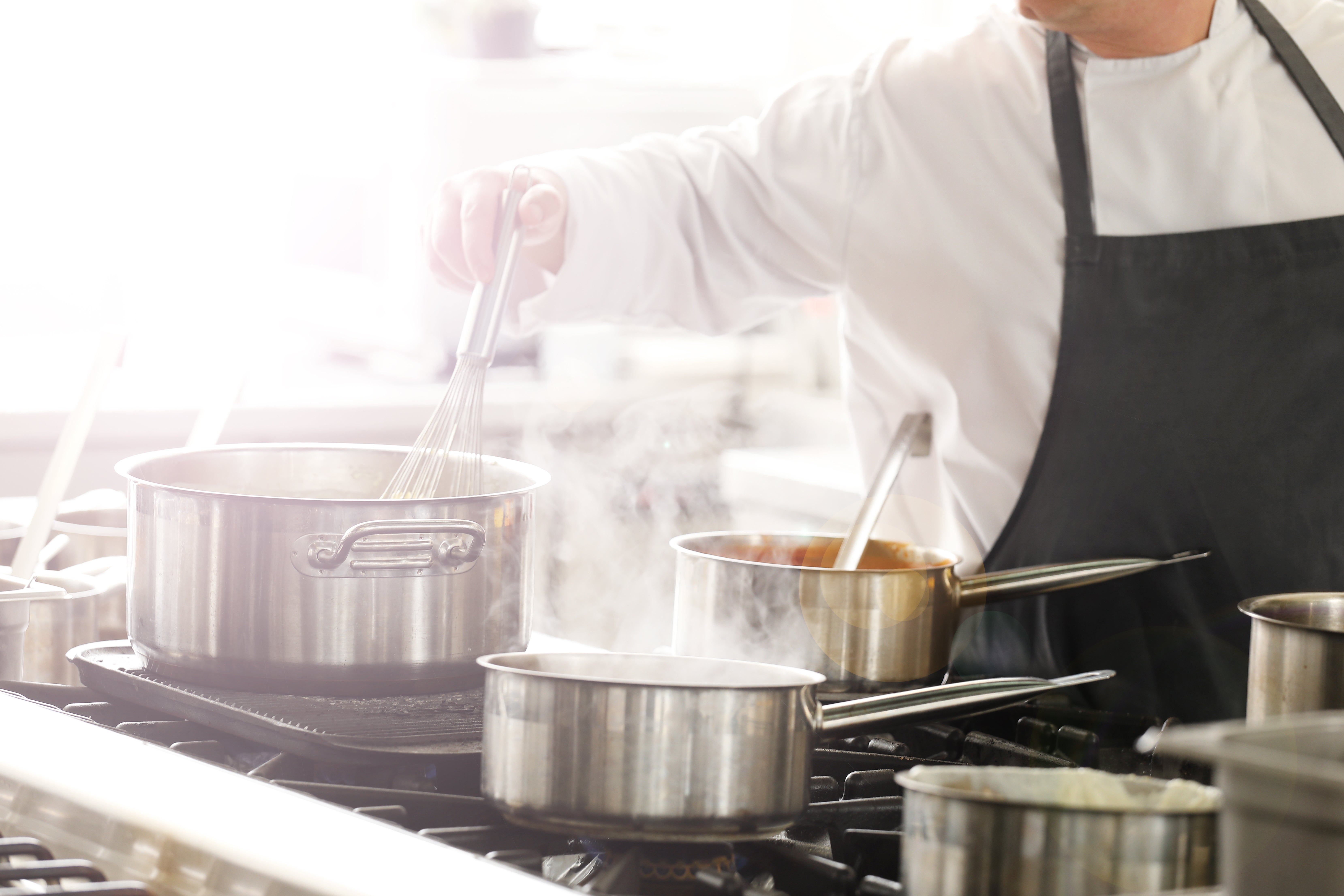 A man wearing a chef's apron is cooking in a modern kitchen, surrounded by utensils and fresh ingredients.