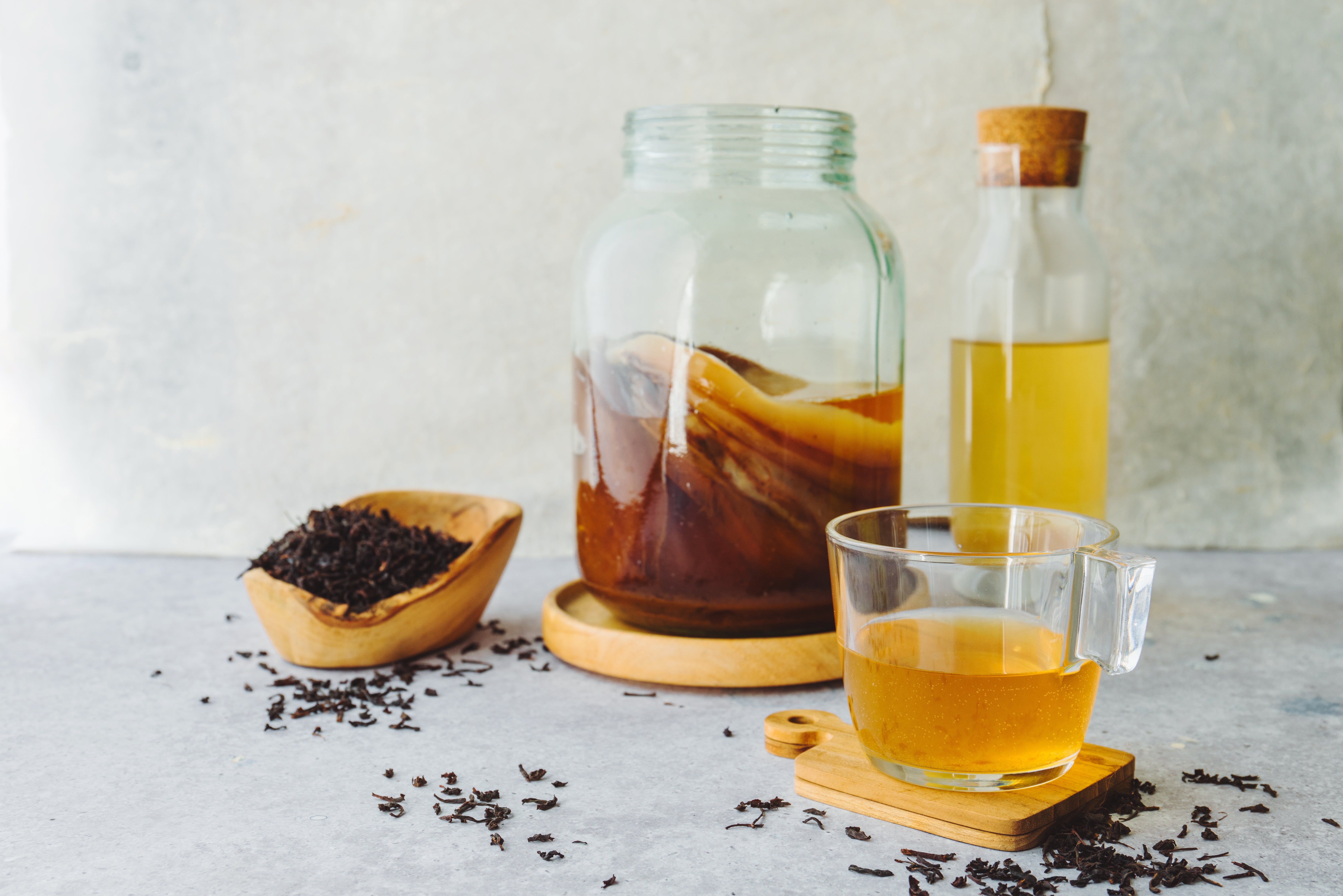 Jar of kombucha with tea leaves, glass of tea, and bottle of brewed drink