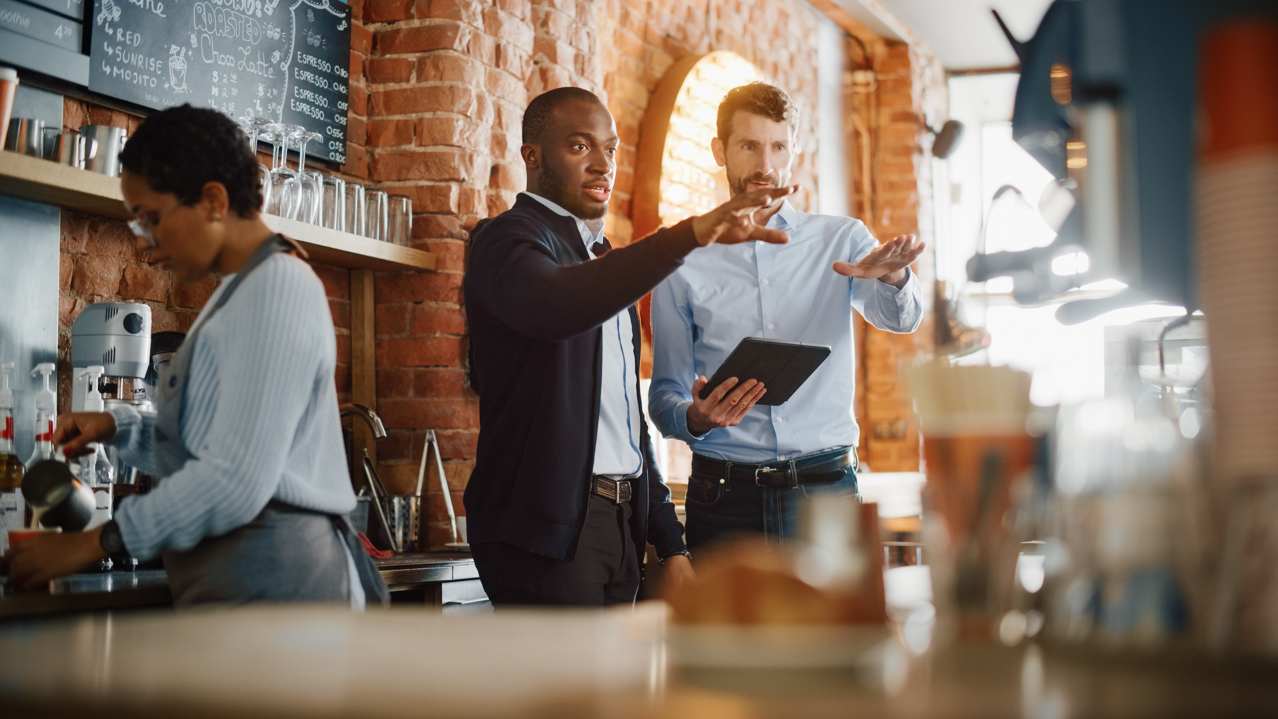 Two men and a woman standing together in a restaurant, discussing the venue's marketing strategies.