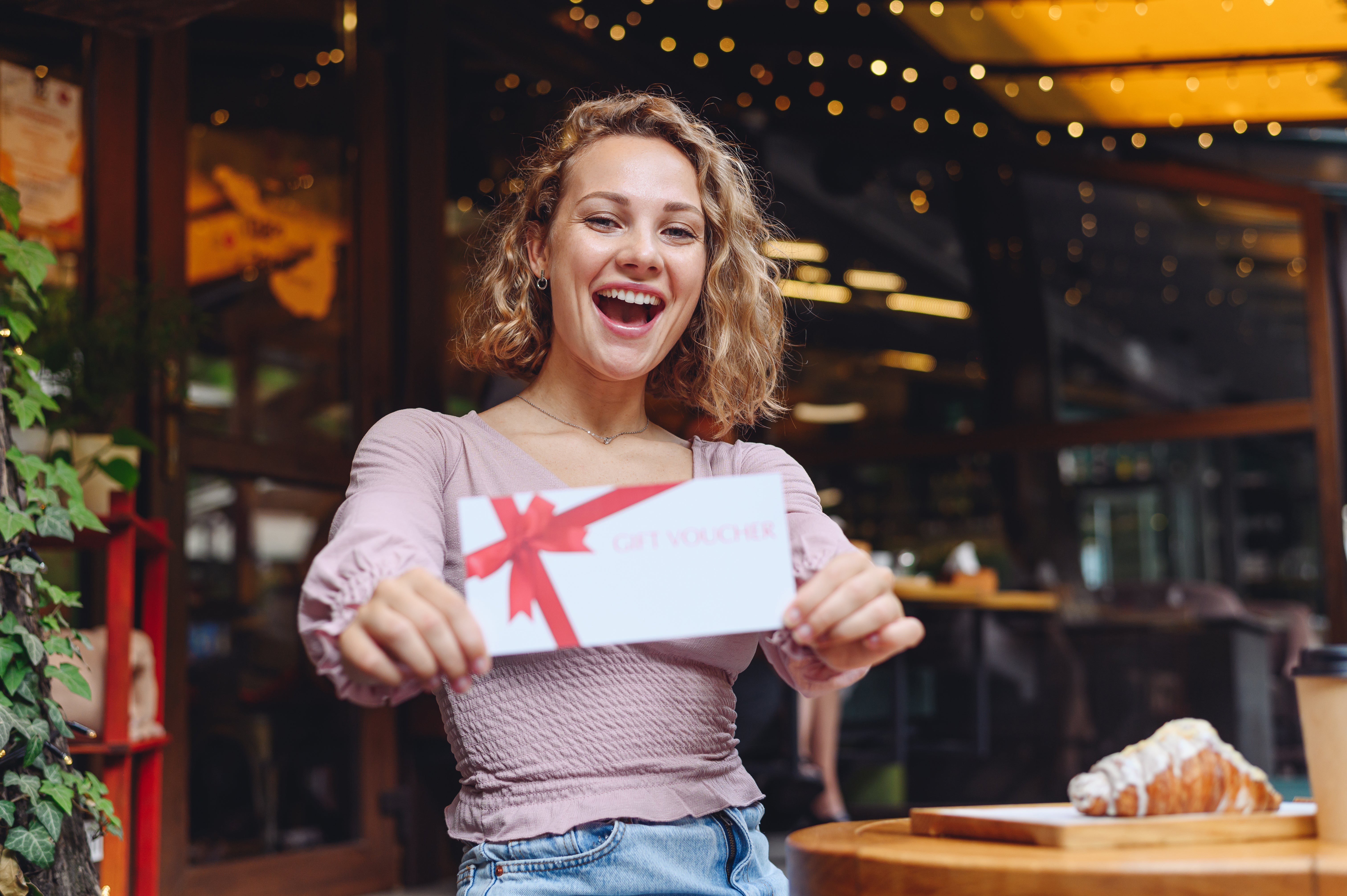 A woman joyfully holds up a gift card, showcasing her excitement and anticipation for the gift inside.