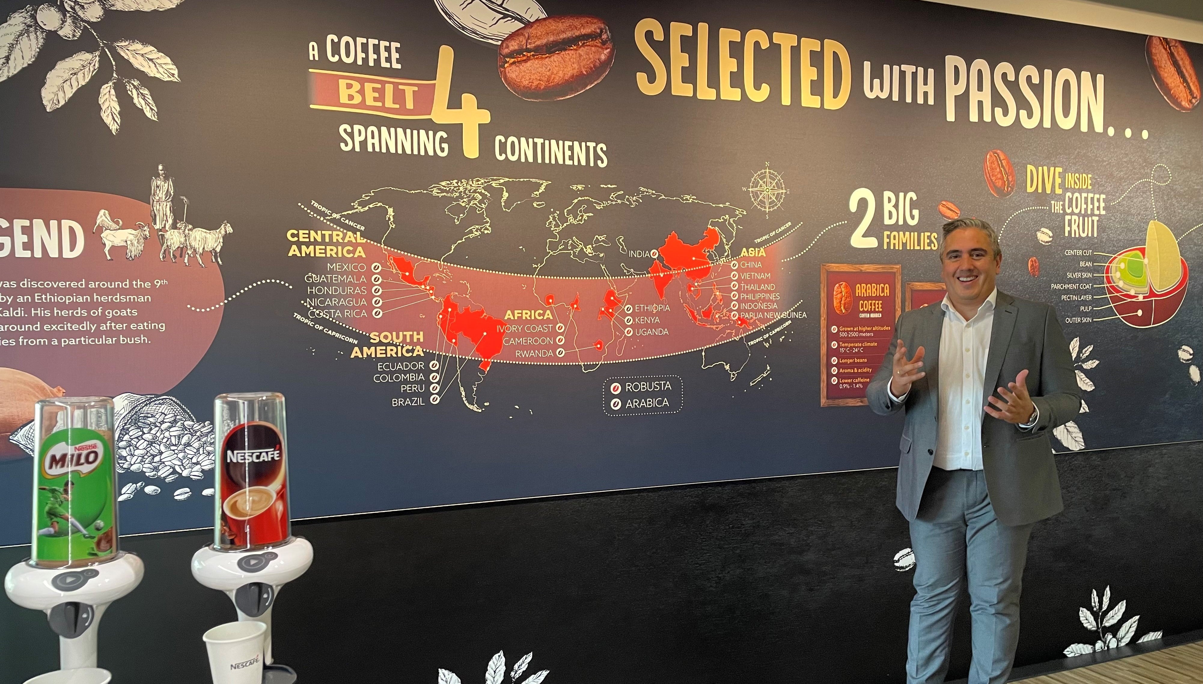 A man stands in front of a wall, next to a coffee machine, ready to brew a fresh cup of coffee.