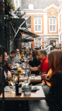 People dining at tables in a lively outdoor restaurant, enjoying food and conversation.