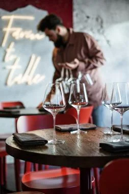 A man is positioned at a table filled with wine glasses, suggesting a social event or toast.
