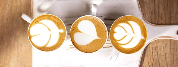 Three cups of coffee with intricate latte art arranged on a rustic wooden table.