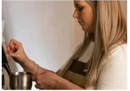 A woman uses a coffee machine to make coffee, focused on her task in a bright kitchen setting.