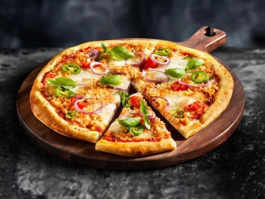A pizza topped with cheese, fresh tomatoes, and basil, presented on a rustic wooden board.