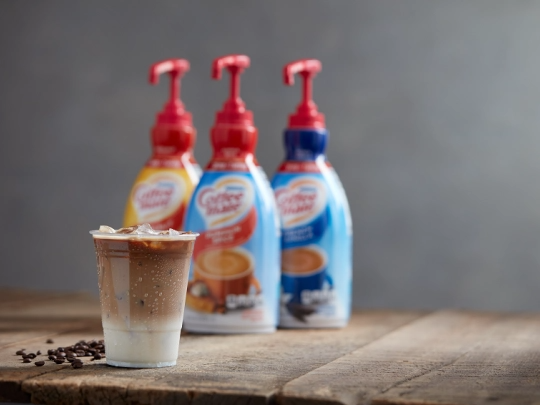 A glass of coffee sits next to a bottle of milk on a wooden table, creating a cozy beverage scene.