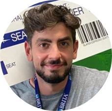 A bearded man wearing a blue badge, smiling and looking confidently at the camera.