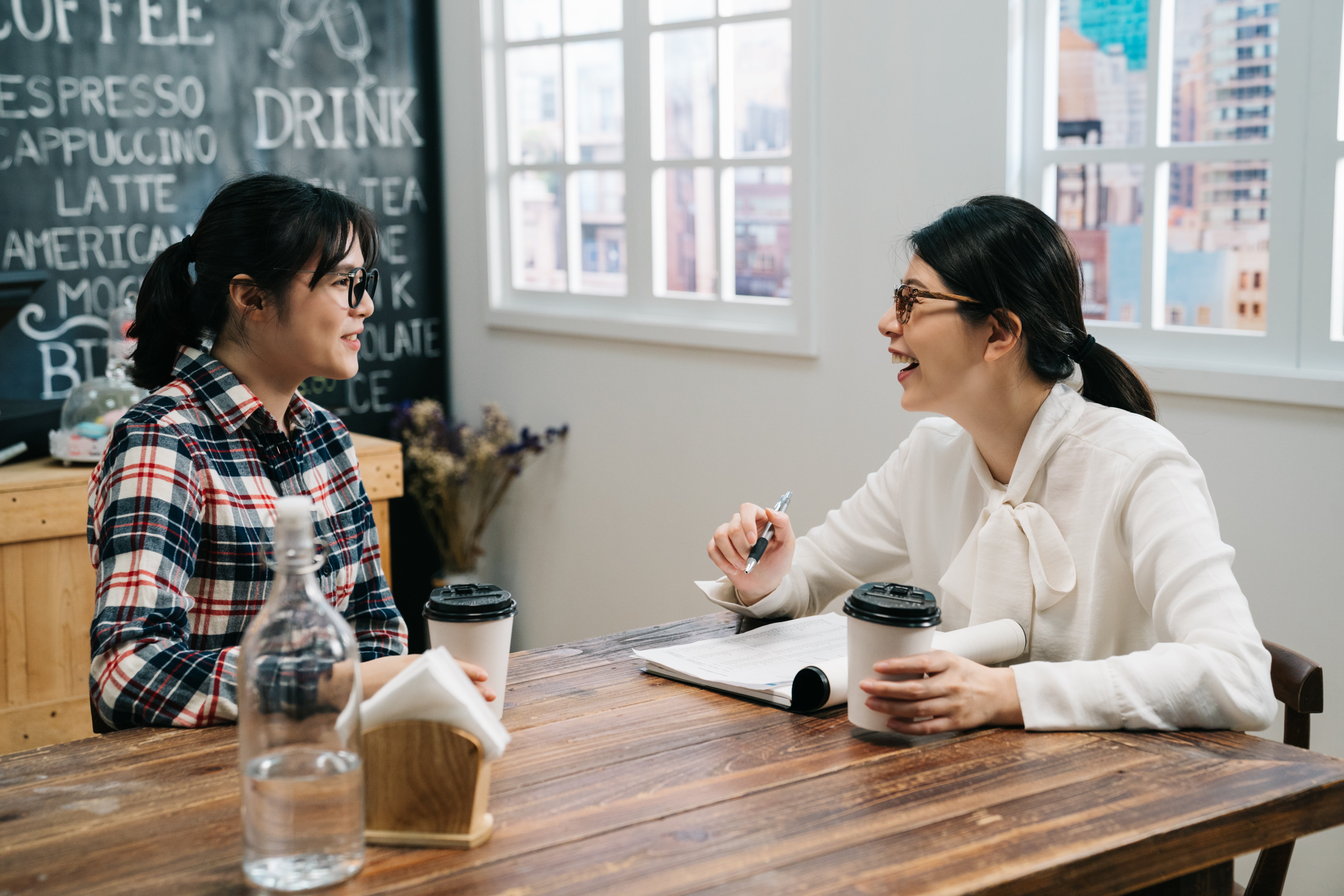 Two women engaged in conversation while sitting at a table, sharing smiles and ideas.