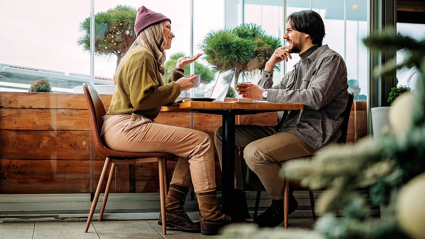 A man and woman seated at a restaurant table, engaged in conversation over a meal.
