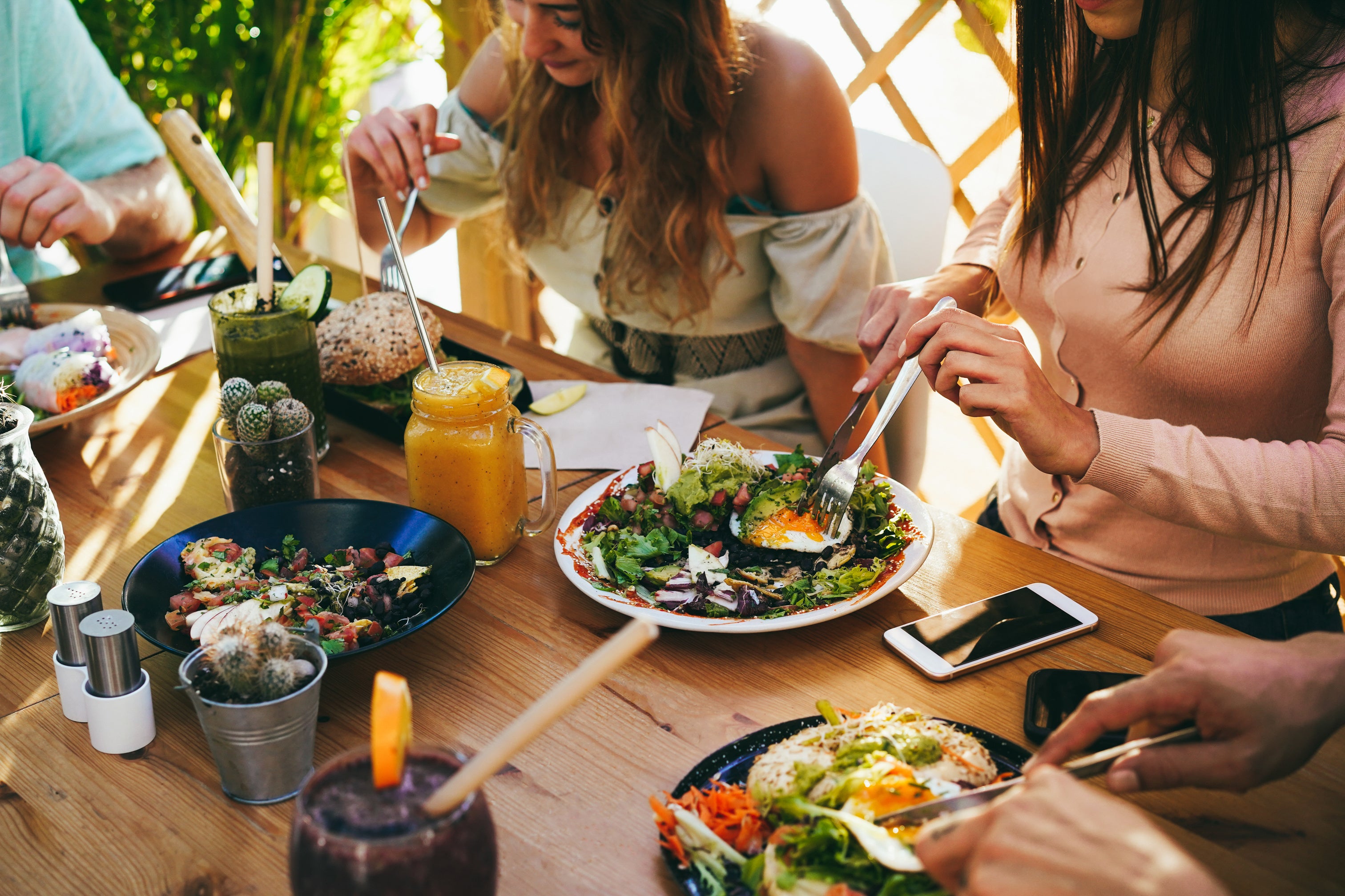 Group of friends enjoying healthy meals and fresh juices at outdoor wooden table
