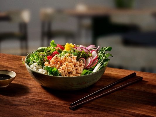 A bowl of fresh salad with chopsticks resting on a wooden table, inviting and ready to be enjoyed.