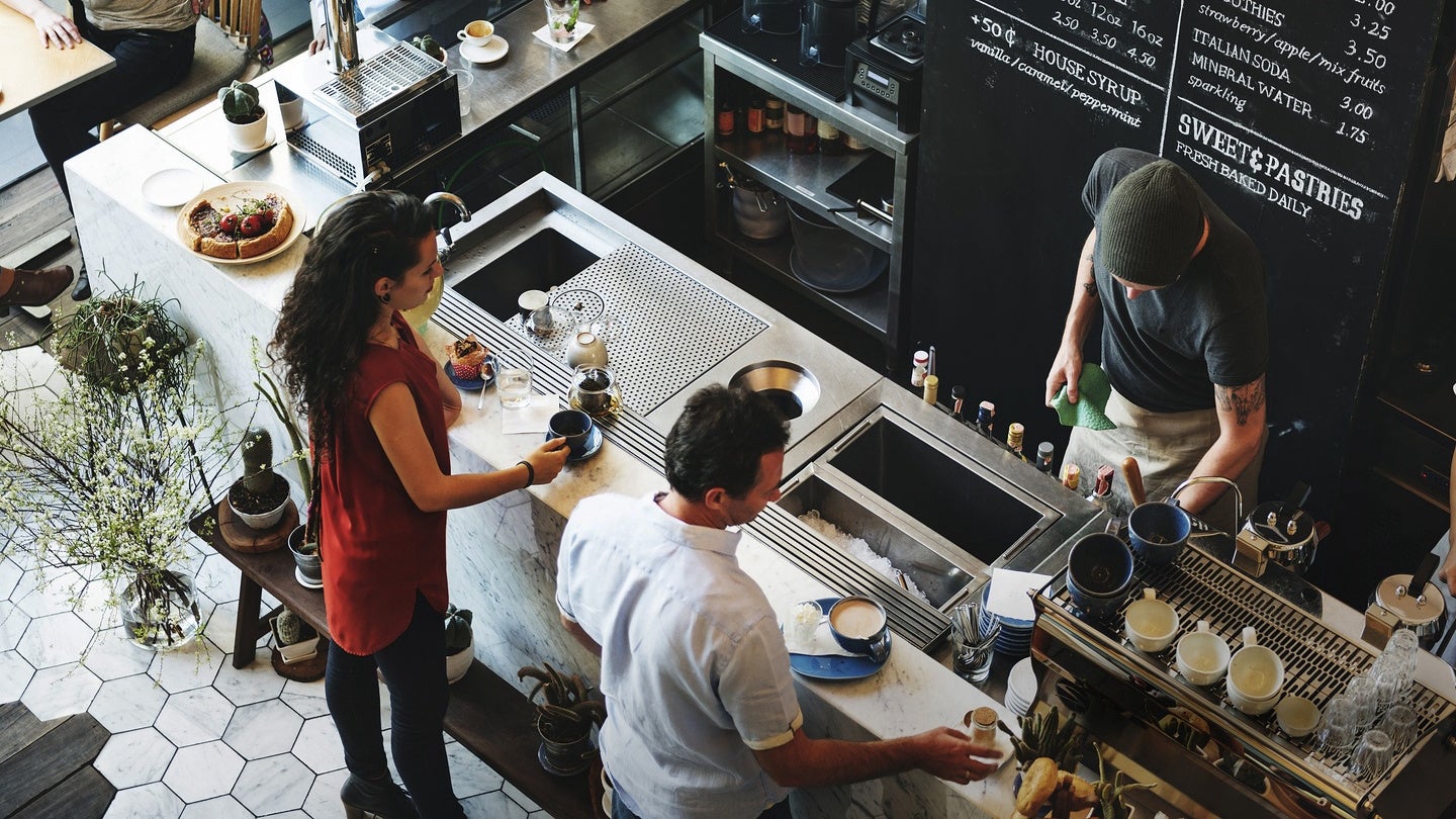 People ordering coffee at a busy café counter with barista preparing drinks.