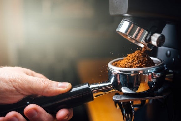A person grinding coffee beans using an espresso machine in a bright kitchen setting.