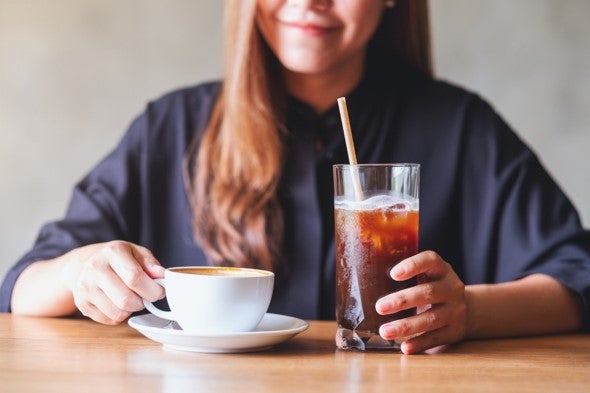 A woman with a cup of coffee and a straw, looking content while sipping her beverage.
