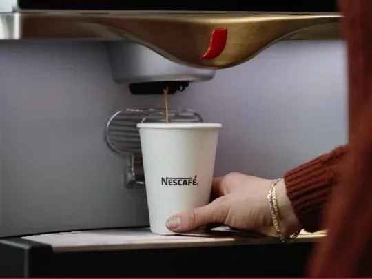 A person holds a steaming cup of coffee, freshly brewed from a coffee machine.