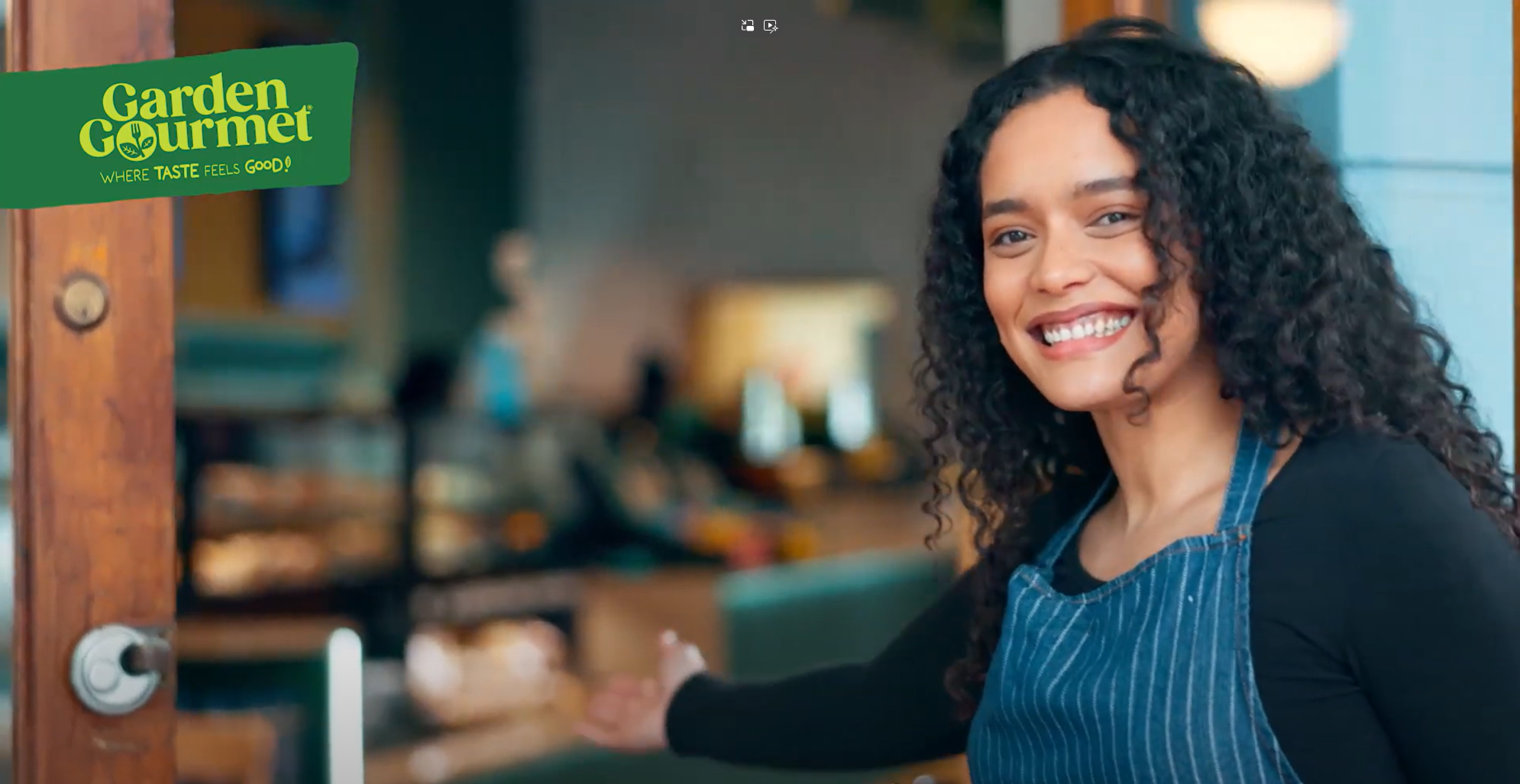 A smiling woman stands in front of a closed door, radiating happiness and warmth.