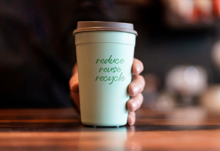A person holds a green cup, promoting the message of reduce, reuse, recycle.
