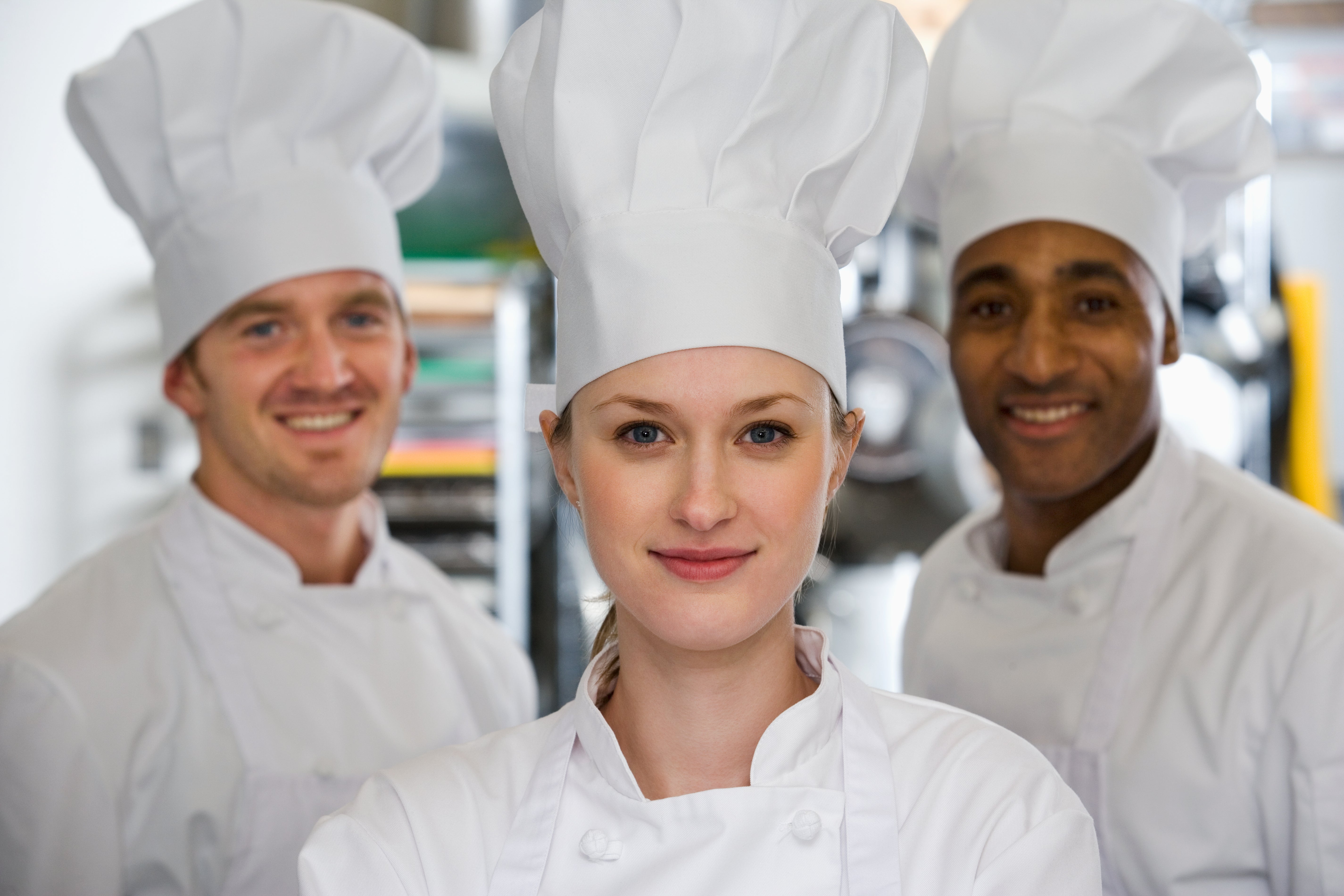 In a well-lit kitchen, three cheerful chefs pose together, exuding a sense of teamwork and culinary passion.