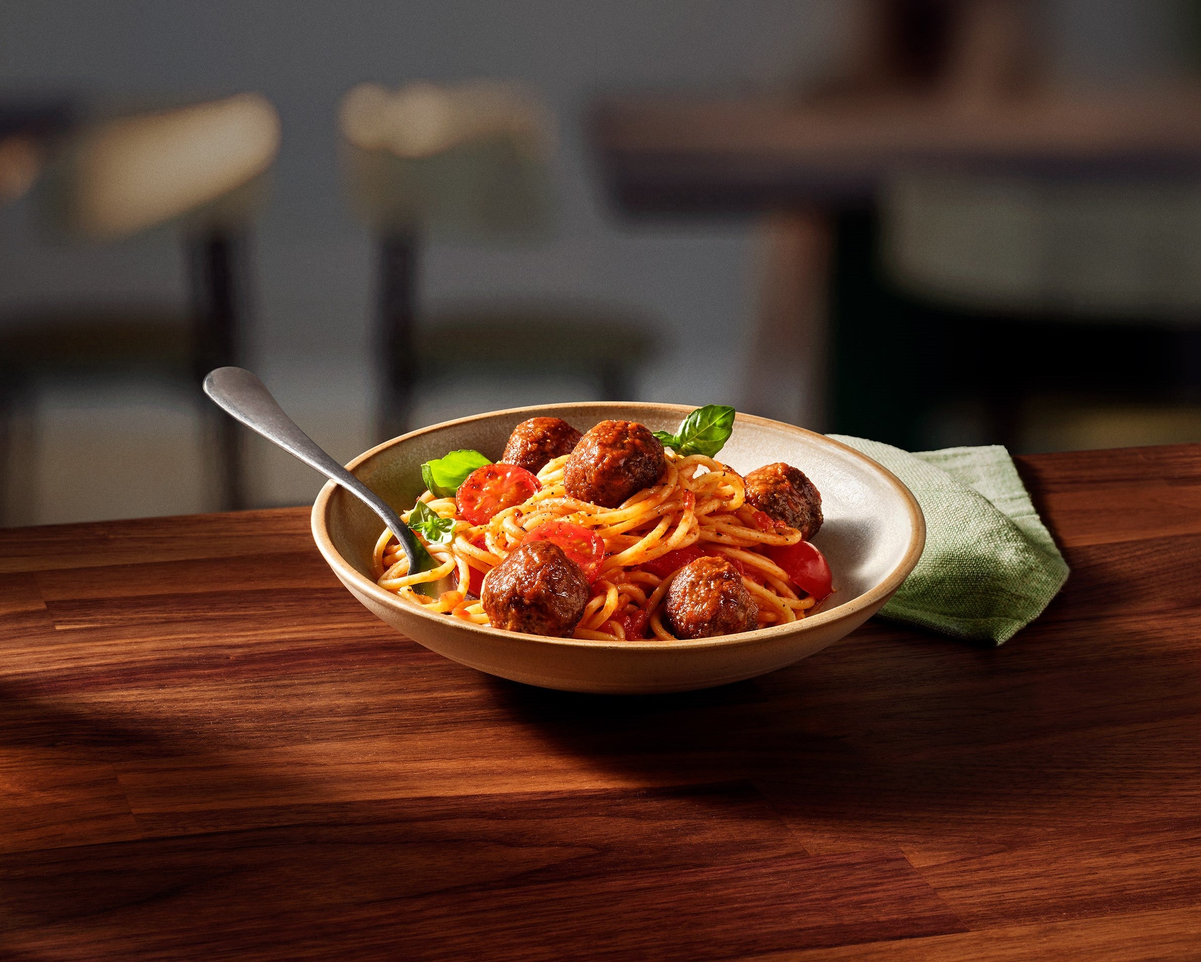 A serving of spaghetti with meatballs and diced tomatoes in a white bowl, showcasing a hearty Italian dish.