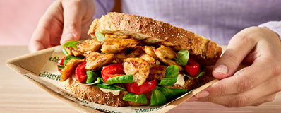 A hand presenting a sandwich filled with chicken and spinach, featured in the Garden Gourmet Plant Proteins Recipes Booklet